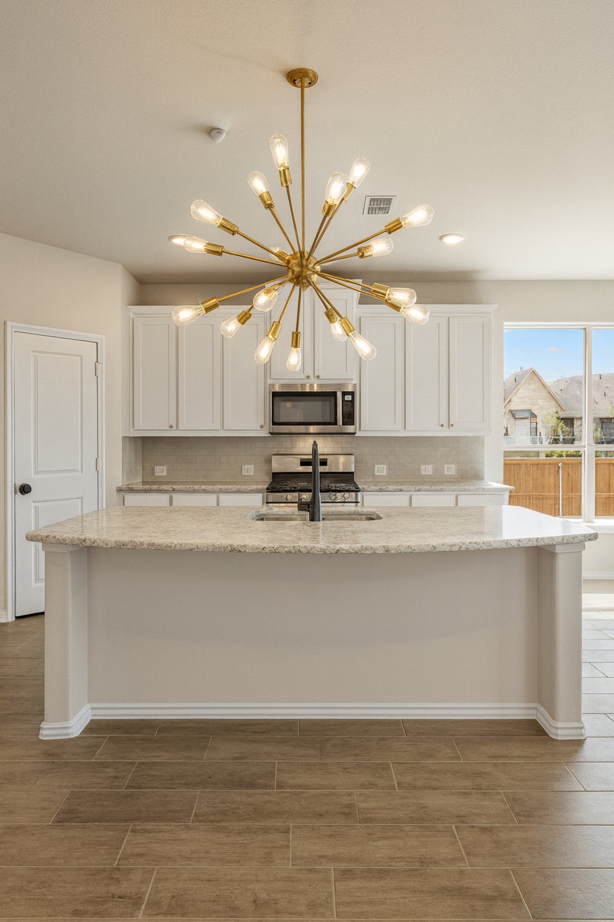 Modern kitchen with a gold chandelier, marble island, and white cabinets.